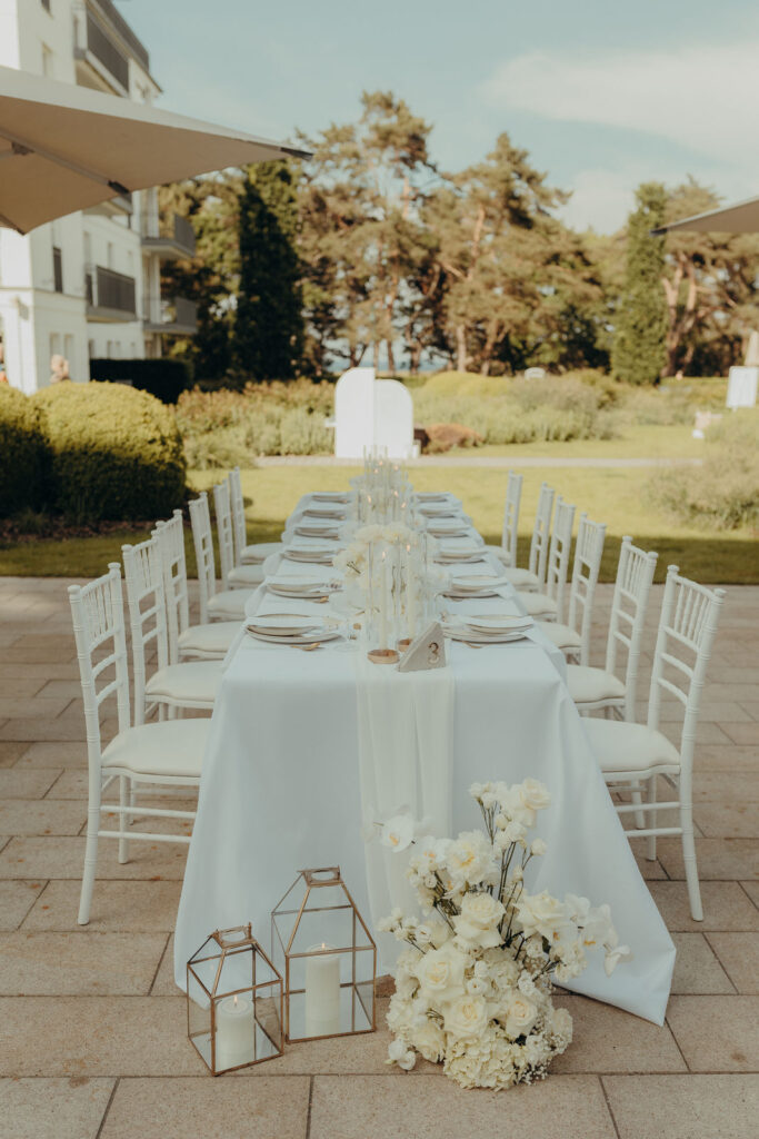 Ein elegant gedeckter Tisch im Freien mit weißen Stühlen, Blumen und Kerzen schafft eine zauberhafte Gartenkulisse - perfekt für einen Hochzeitsplaner in Rostock an der Ostsee - Wedding Planner Vanessas Hochzeitszauber