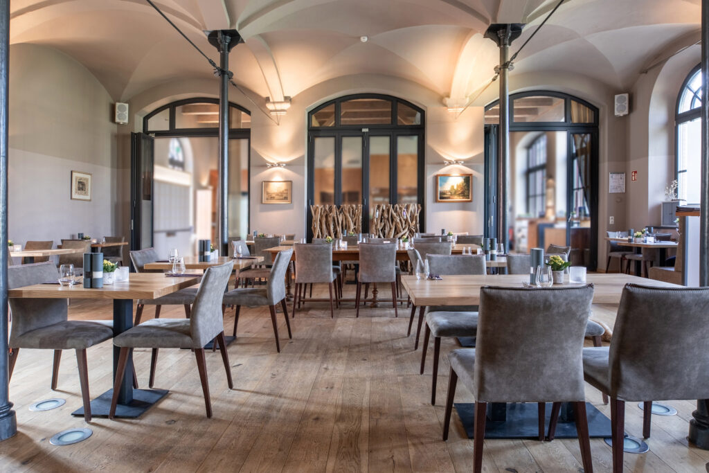 Elegantes Restaurant-Interieur mit Holzböden, modernen Tischen, grauen Stühlen und großen Bogenfenstern - eine ideale Hochzeitslocation nahe der Ostsee in Mecklenburg-Vorpommern.