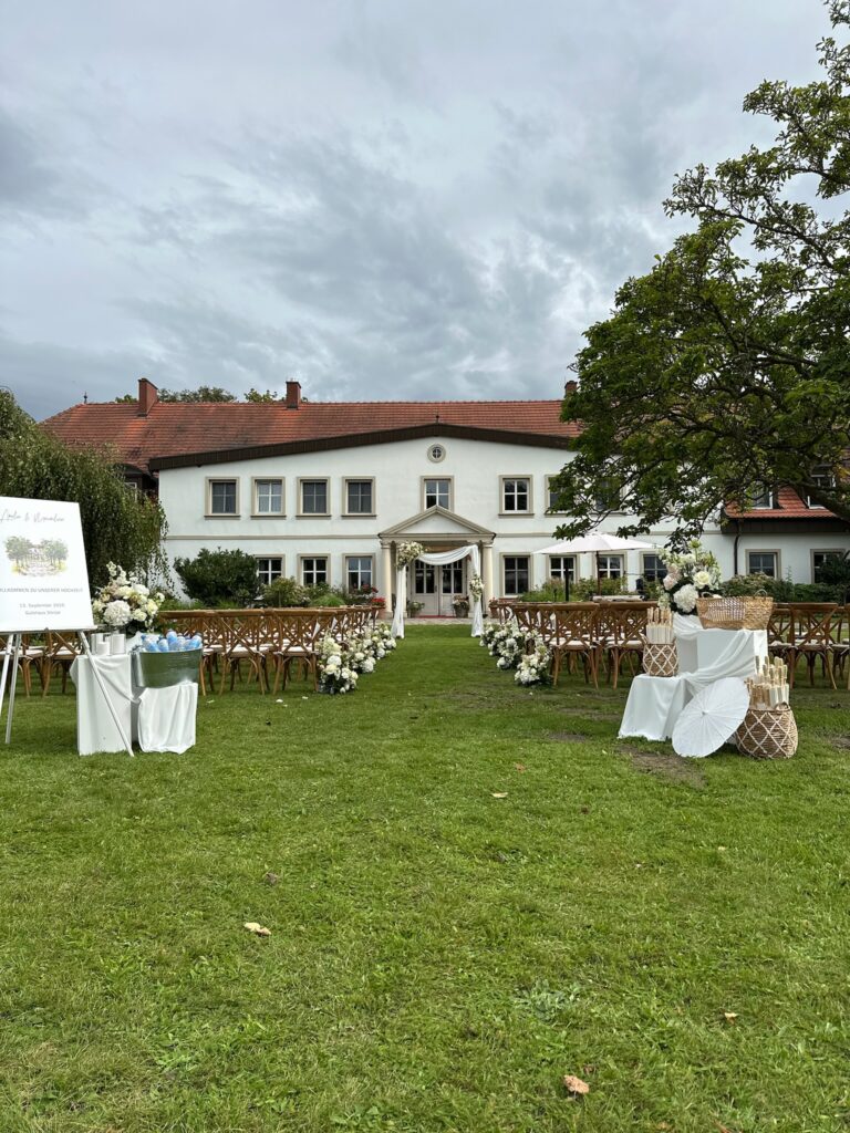 Hochzeit im Freien mit Stühlen, Blumendekoration und einem weißen Gebäude im Hintergrund bei bewölktem Himmel in einer charmanten Hochzeitslocation in Mecklenburg-Vorpommern nahe der Ostsee.