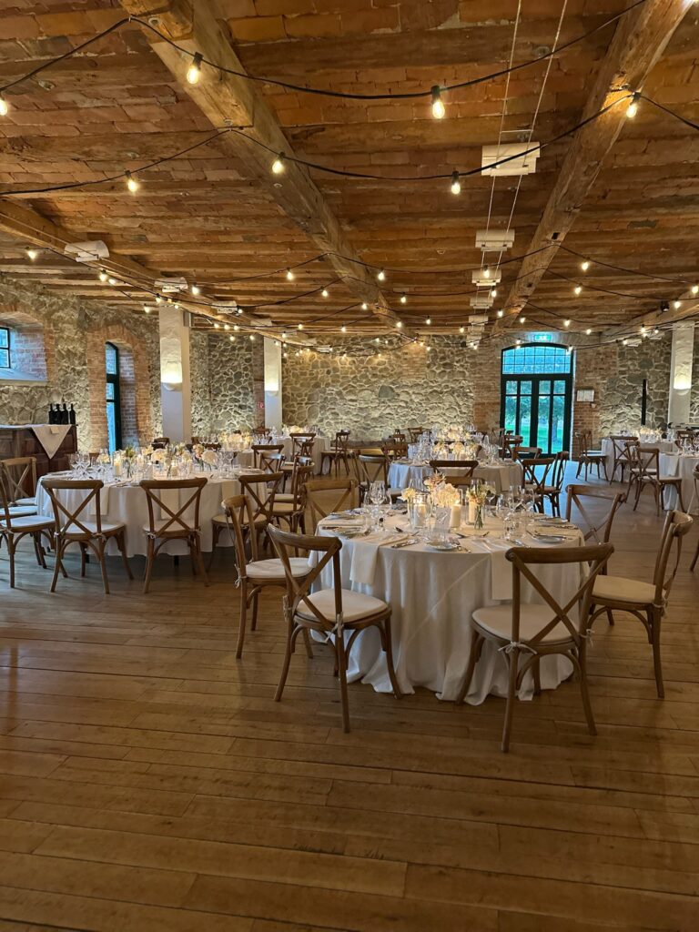 Eleganter Festsaal mit runden Tischen, Holzstühlen, Lichterketten und Steinmauern für eine Veranstaltung vorbereitet - eine ideale Hochzeitslocation in Mecklenburg-Vorpommern nahe der Ostsee.