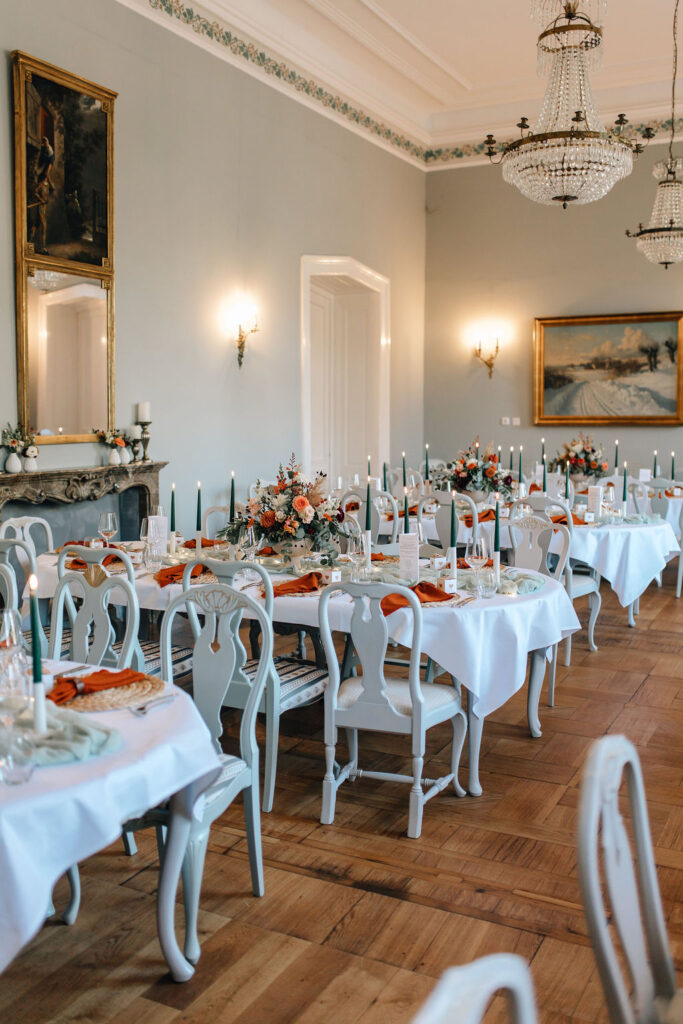 Eleganter Speisesaal mit weißen Tischen, floralen Tafelaufsätzen, Kerzen und Vintage-Kronleuchtern - eine bezaubernde Hochzeitslocation in Mecklenburg-Vorpommern nahe der Ostsee.