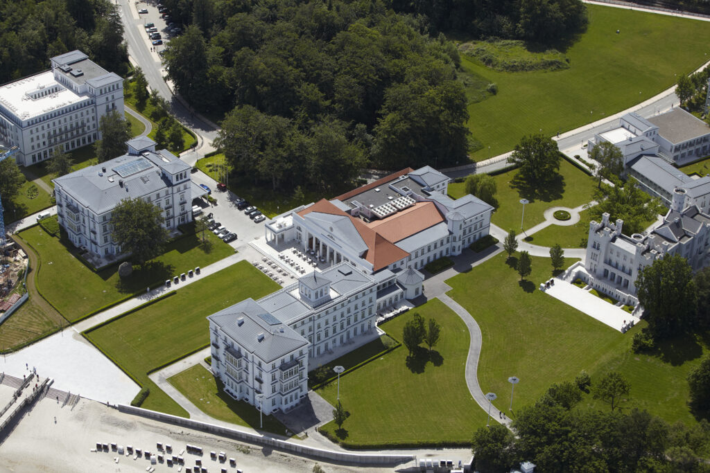Luftaufnahme mehrerer großer weißer Gebäude, umgeben von grünen Rasenflächen und Bäumen in der Nähe der Ostsee, die eine malerische Kulisse für eine Hochzeitslocation in Mecklenburg-Vorpommern bieten.